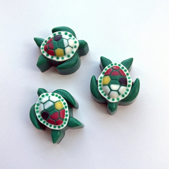 Three green turtle-shaped chocolates with colourful shell designs, customized using corporate logo colours.