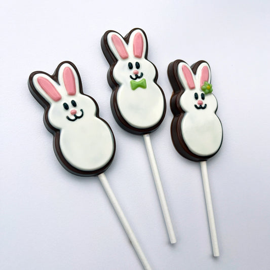 Three chocolate bunnies on sticks, adorned with white bodies, pink ears and noses, happy smiles, a bowtie or flower.