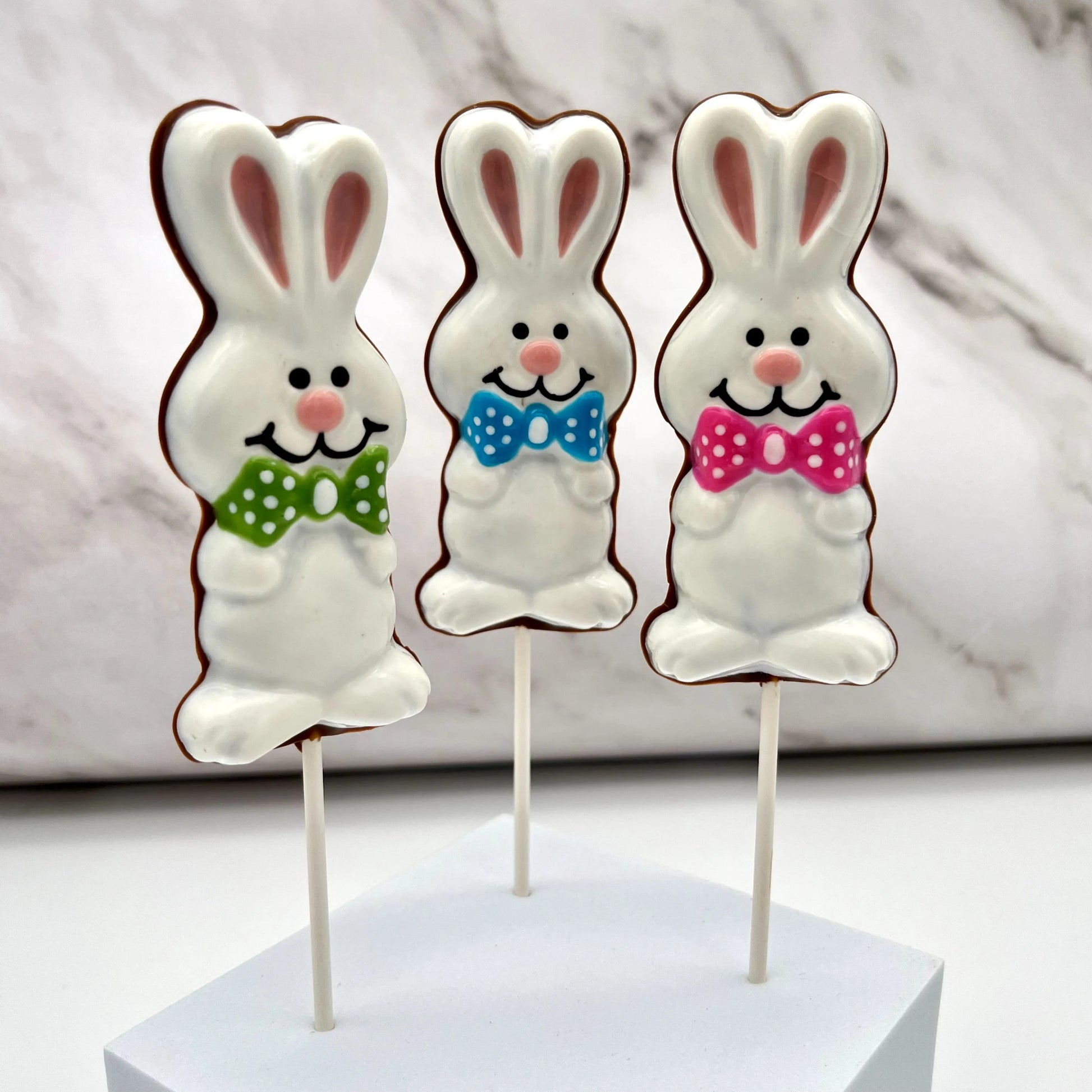 Easter Bunny suckers coloured in white and pink, adorned with polka dot bowties in pink, green or blue. Filled with milk chocolate.