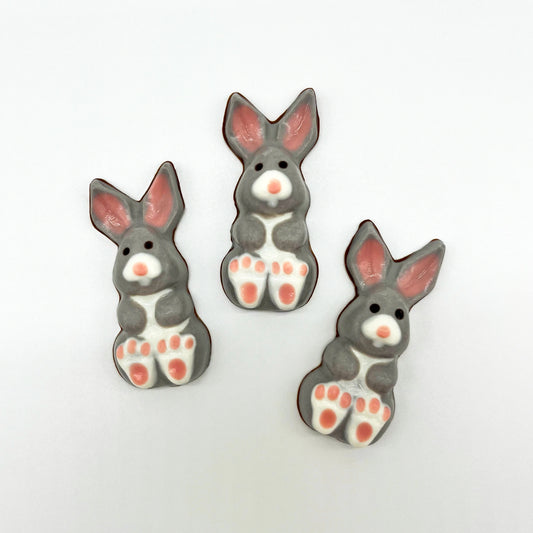 Three grey and white chocolate bunnies with little pink toes and ears, sitting in a cute posture.