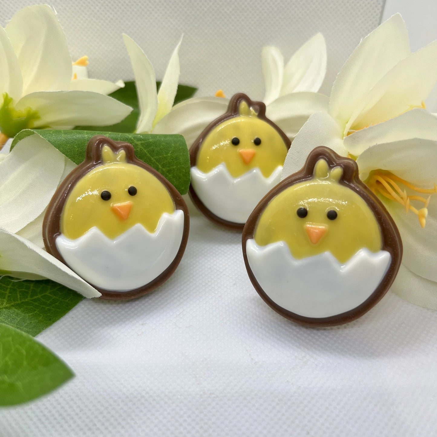 Round emoji-style yellow chicks sitting in white eggs, filled with milk chocolate, creating a nice contrast border.