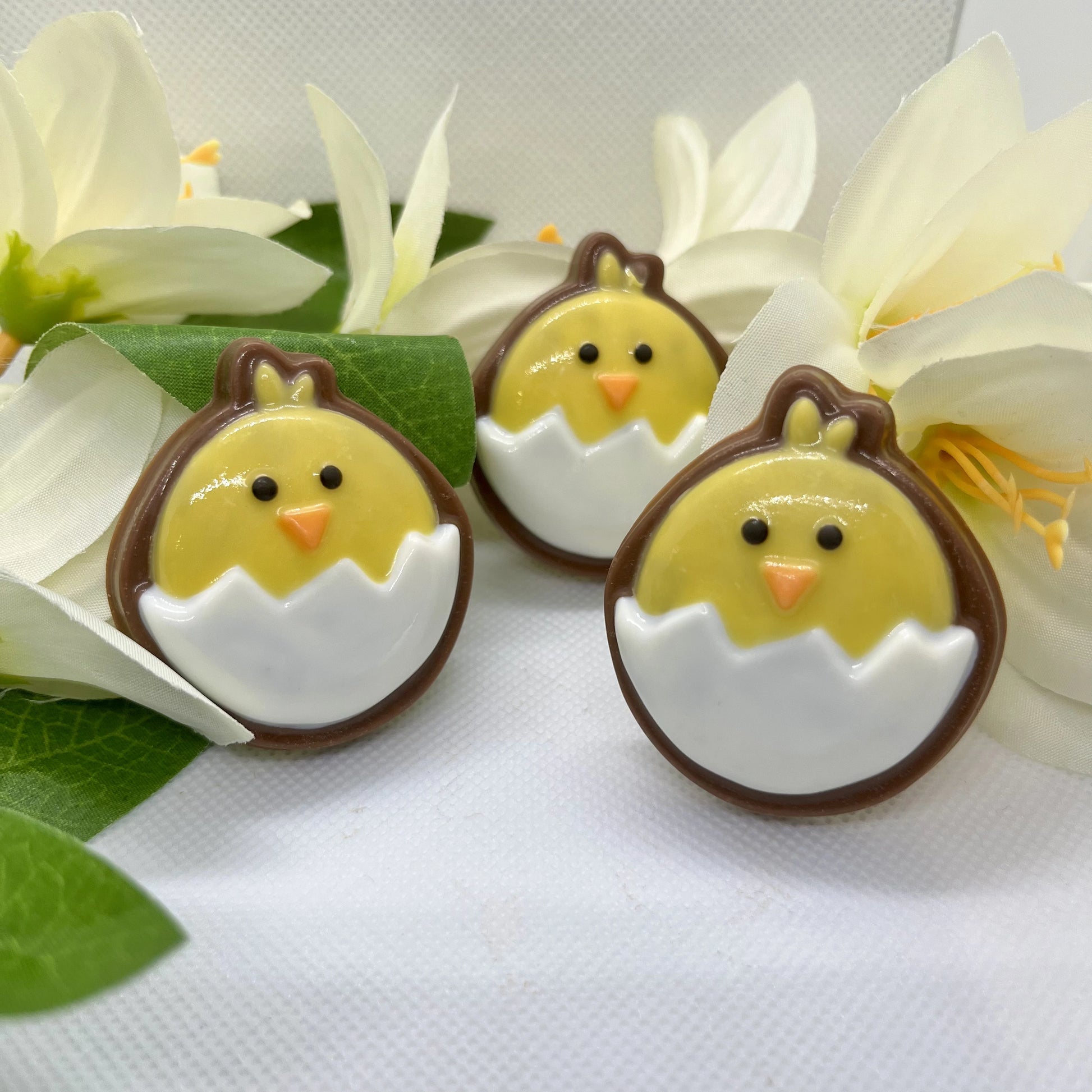 Round emoji-style yellow chicks sitting in white eggs, filled with milk chocolate, creating a nice contrast border.