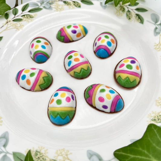 A plate full of chocolate Easter eggs decorated with zigags, stripes and dots in 7 vibrant colours.