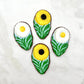 Chocolate white daisies and yellow daisies, with green leaves on a clear blue background, resembling field daisies.