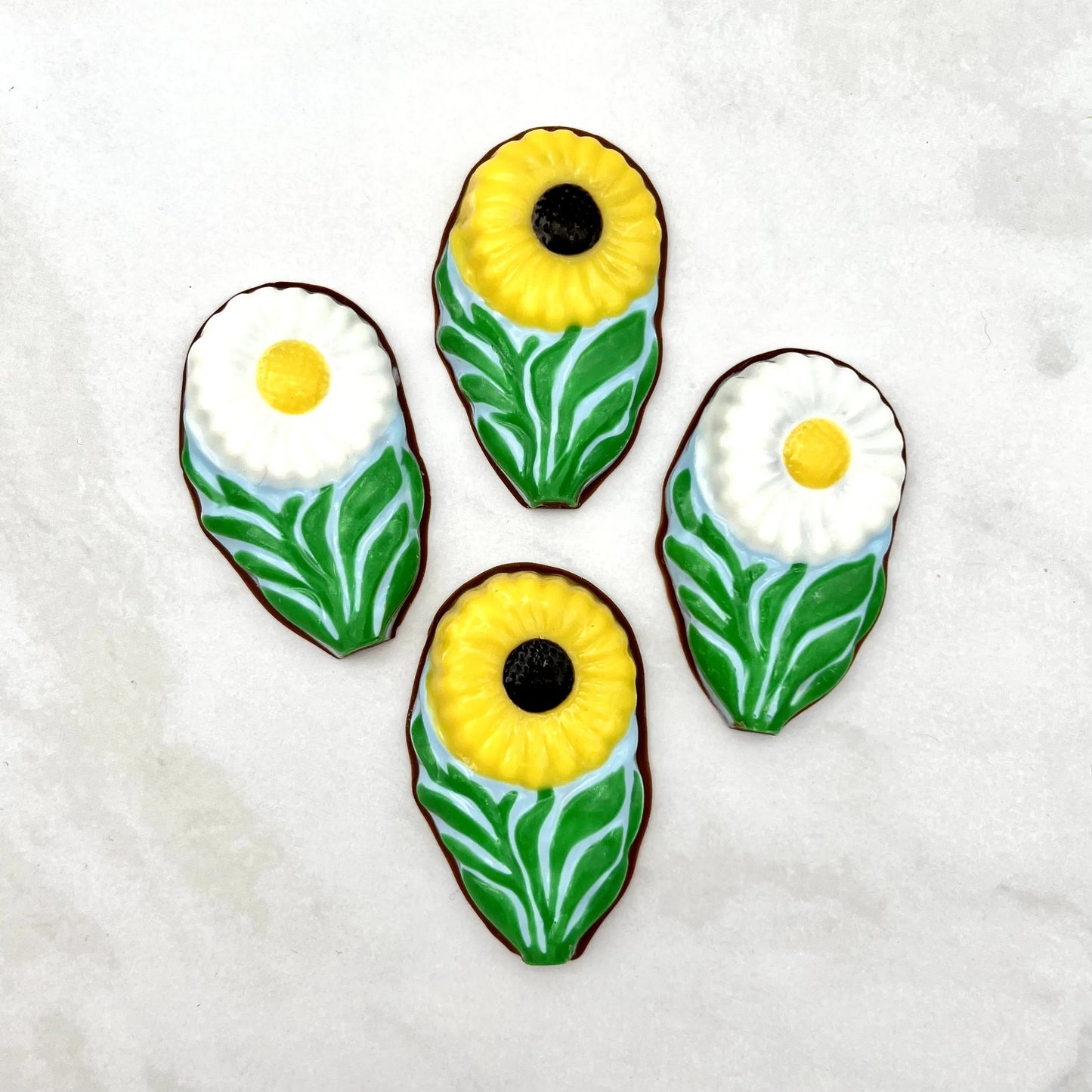 Chocolate white daisies and yellow daisies, with green leaves on a clear blue background, resembling field daisies.