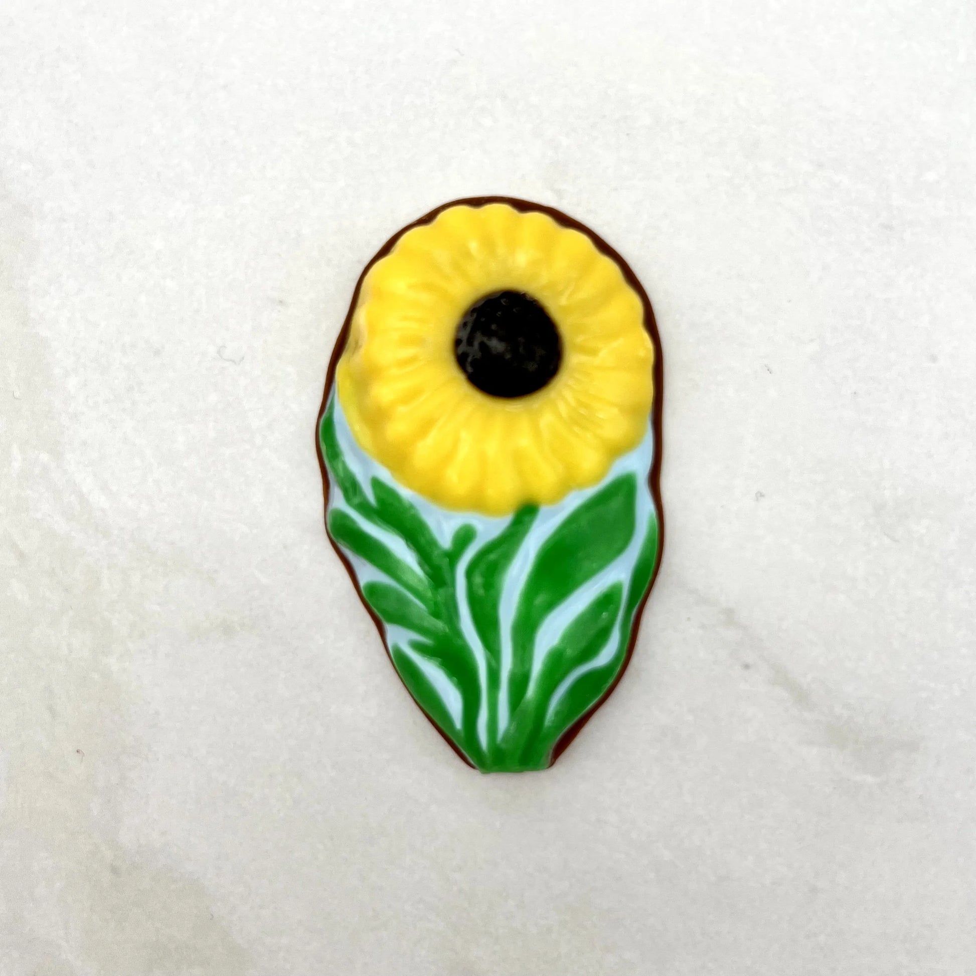 Yellow daisies with black centres, with green leaves on a clear blue background, resembling field daisies.