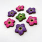 8 chocolate forget-me-not flowers in vibrant purple, pink and green, all with black and yellow centre.