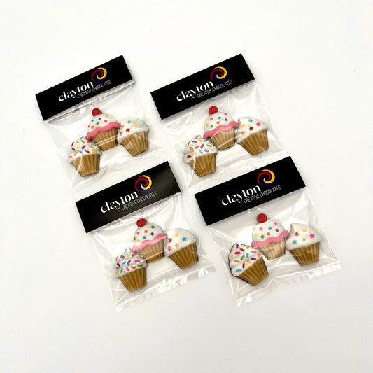 Little cupcakes made from chocolate, packaged in sets of three. Decorated with sprinkles, stars and dots on white icing, in beige cups.