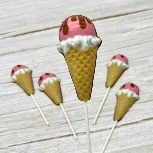 Ice cream cone chocolate suckers decorated in neopolitan colours; light brown cone, candy-sprinkled white, bright pink, topped with brown dripping like melting chocolate.