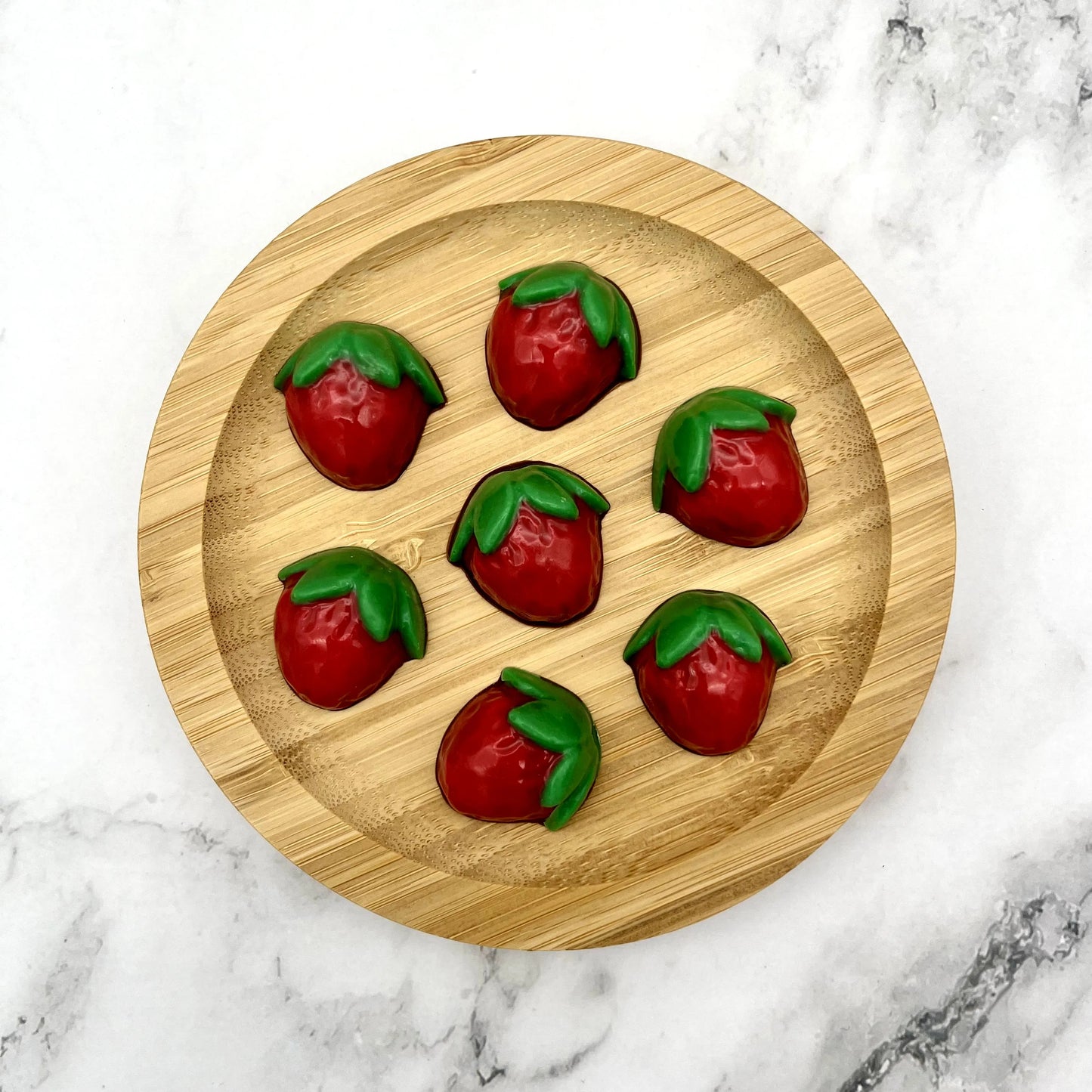 Cute red and green coloured chocolate strawberries on a wooden plate.