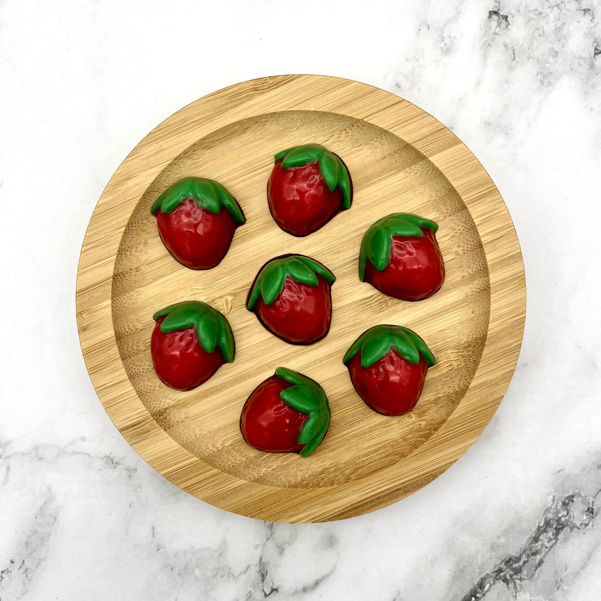 Cute red and green coloured chocolate strawberries on a wooden plate.