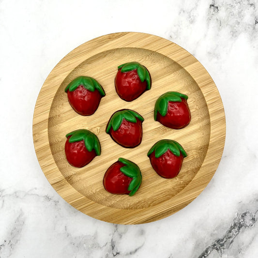 Cute red and green coloured chocolate strawberries on a wooden plate.