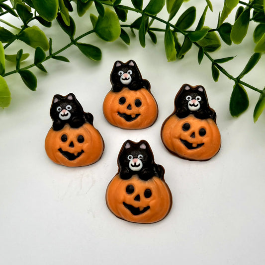Four chocolates of orange pumpkins with carved faces with black and white cats on top.