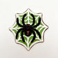 Jumbo black widow spider chocolate, painted with red eyes and hourglass marking, sitting on a white web on a green  background.