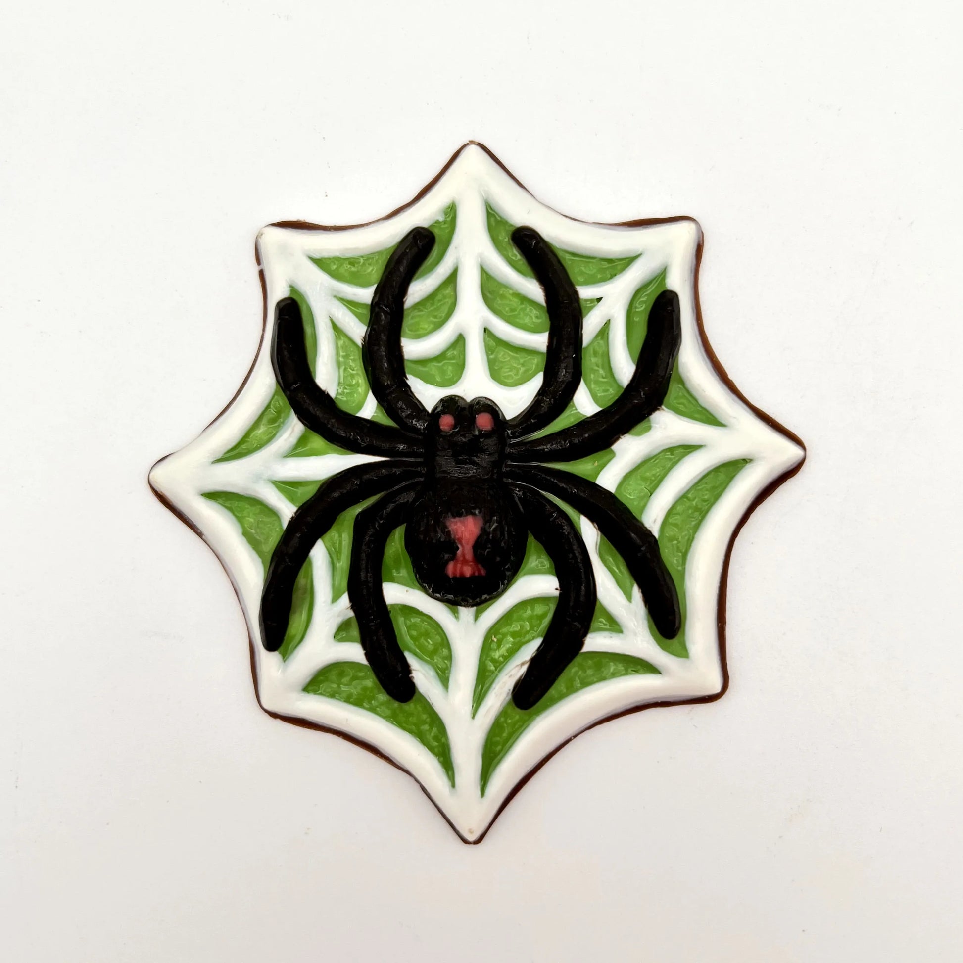Jumbo black widow spider chocolate, painted with red eyes and hourglass marking, sitting on a white web on a green  background.