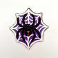 Jumbo black widow spider chocolate, painted with red eyes and hourglass marking, sitting on a white web on a purple  background.