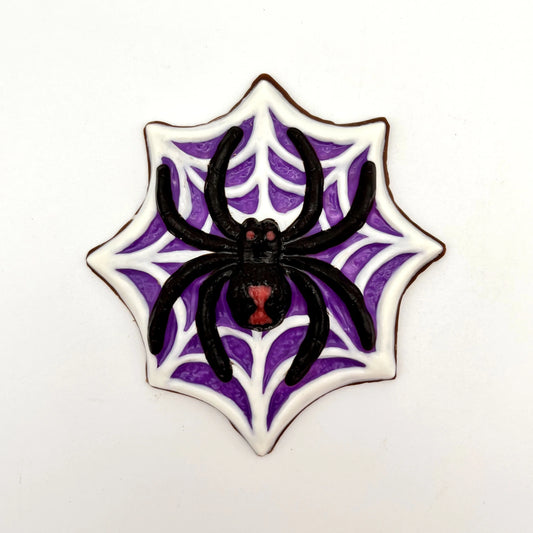 Jumbo black widow spider chocolate, painted with red eyes and hourglass marking, sitting on a white web on a purple  background.