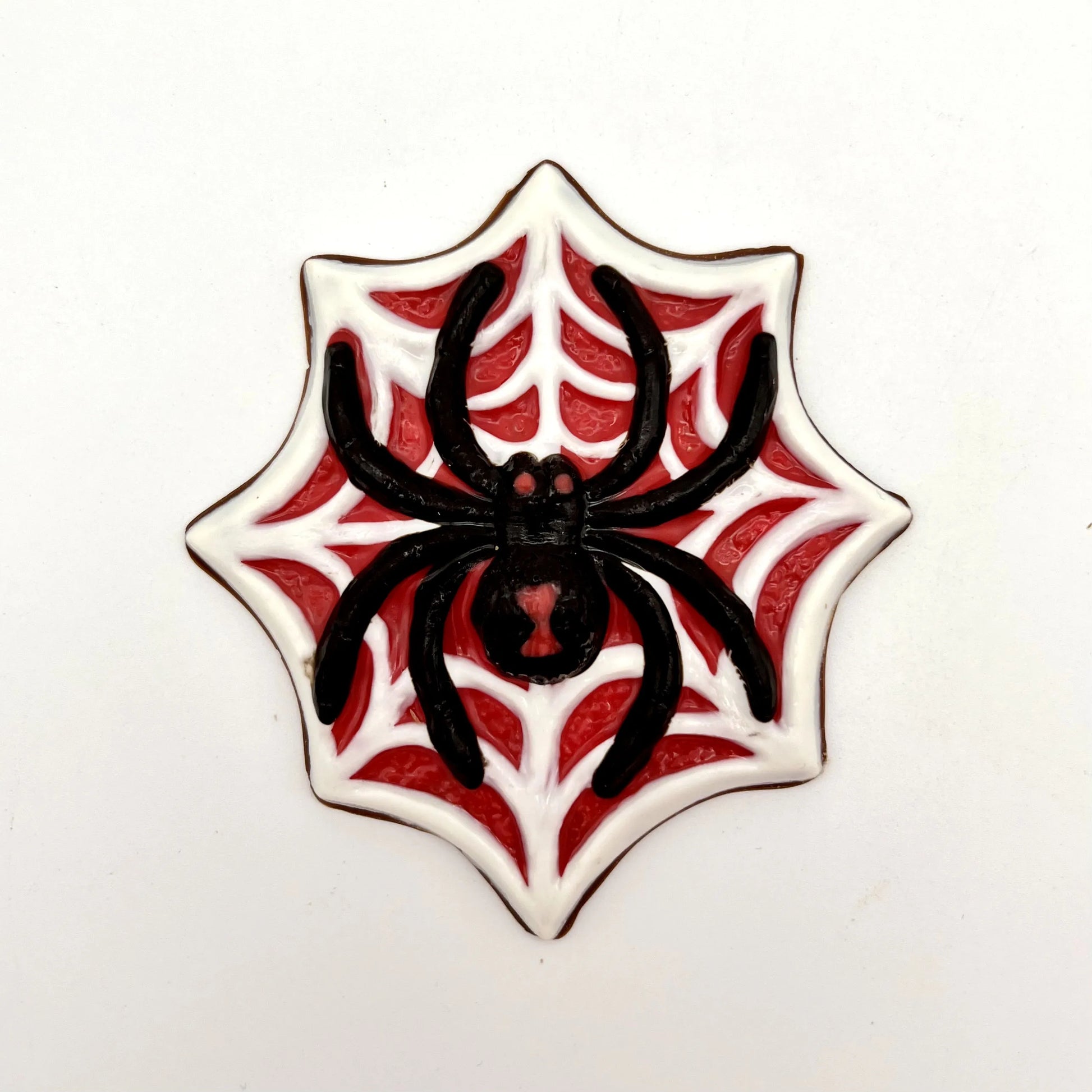 Jumbo black widow spider chocolate, painted with red eyes and hourglass marking, sitting on a white web on a red  background.