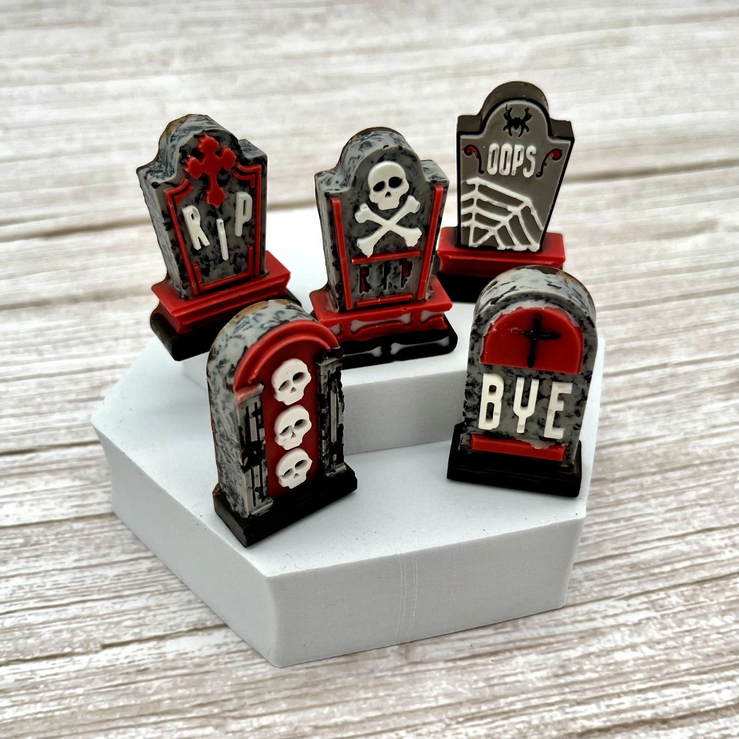 Set of chocolate Halloween-themed tombstones in black, red and grey, displayed on a white base with a wooden background.