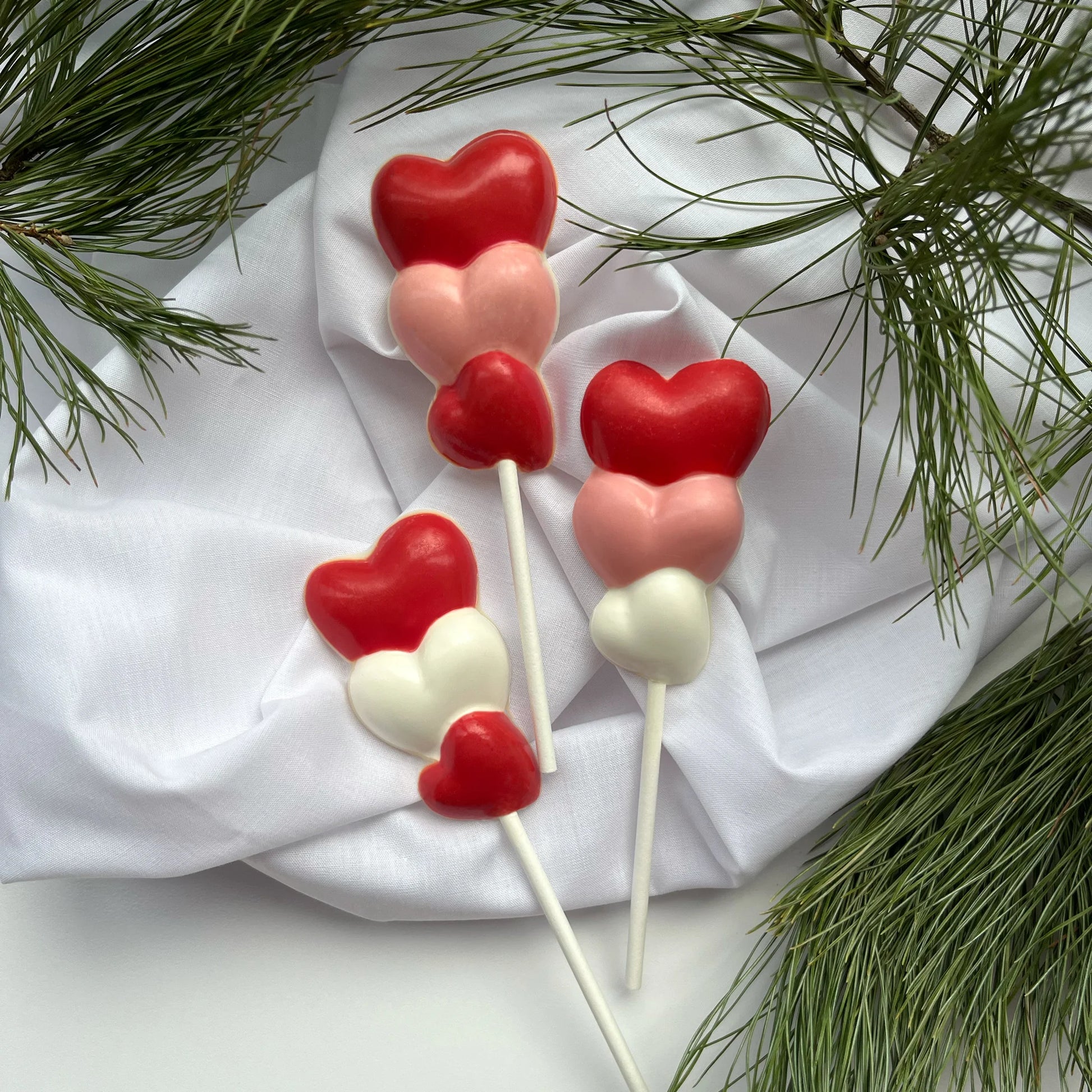 Three hearts stacked on top of each other, on a stick as a chocolate sucker. Variations of white, pink and red on each.