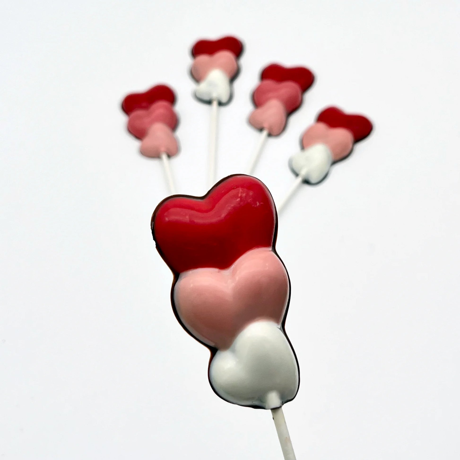 Three hearts stacked on top of each other, on a stick as a chocolate sucker. Variations of white, pink and red on each.