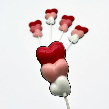 Three hearts stacked on top of each other, on a stick as a chocolate sucker. Variations of white, pink and red on each.