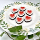 Heart-shaped chocolates on a wooden board, each with a white outer heart and a red heart centre surrounded by a pink border. 