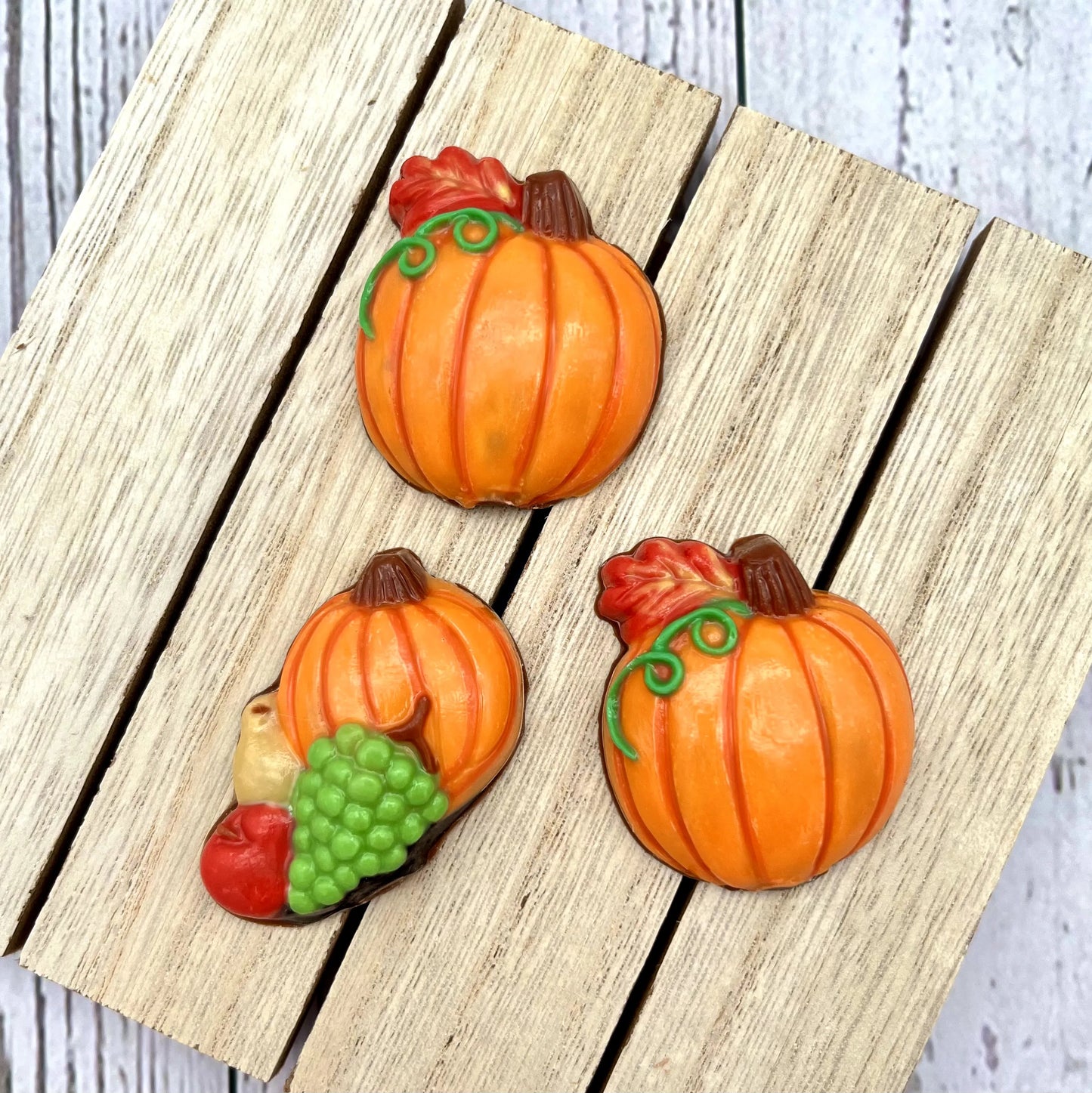 Fall-themed chocolate pumpkins. Two with green tendrils paired with autumn oak leaves, and one with grapes, an apple and a pear.