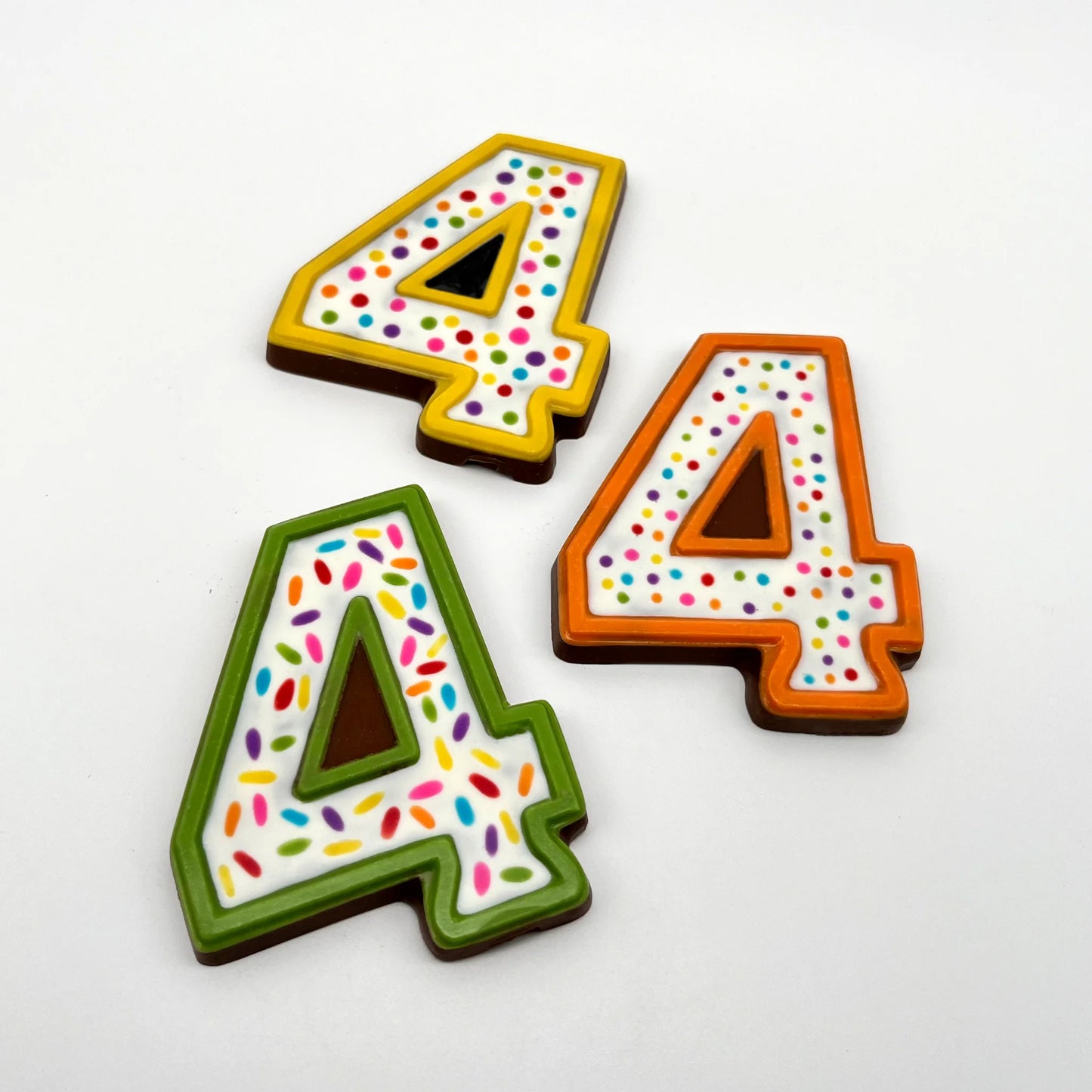 Three colourful number '4' chocolates, hand-painted with multi-colour dots and sprinkles. Displayed on a white background.