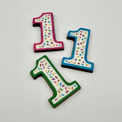 Three colourful number '1' chocolates, hand-painted with multi-colour dots and sprinkles. Displayed on a white background.
