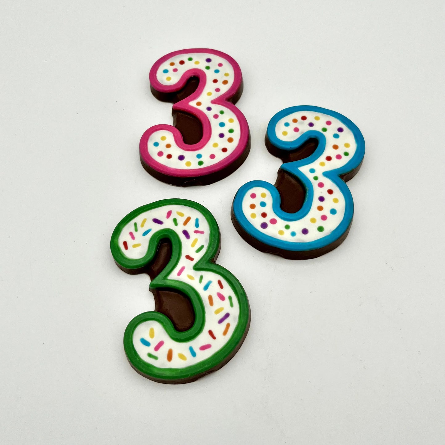 Three colourful number '3' chocolates, hand-painted with multi-colour dots and sprinkles. Displayed on a white background.