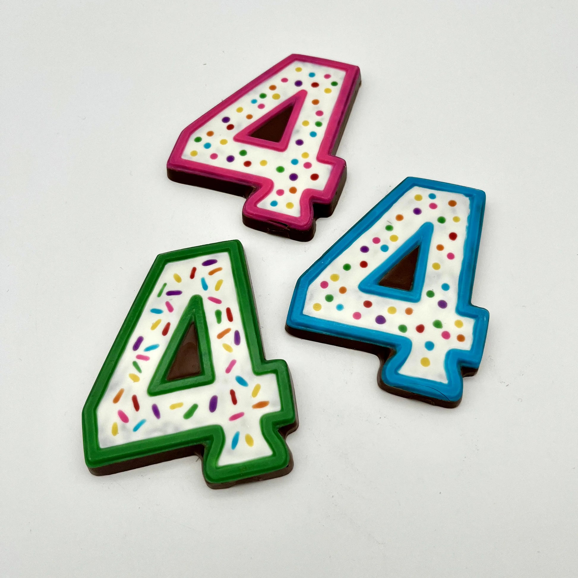 Three colourful number '4' chocolates, hand-painted with multi-colour dots and sprinkles. Displayed on a white background.