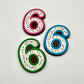 Three colourful number '6' chocolates, hand-painted with multi-colour dots and sprinkles. Displayed on a white background.
