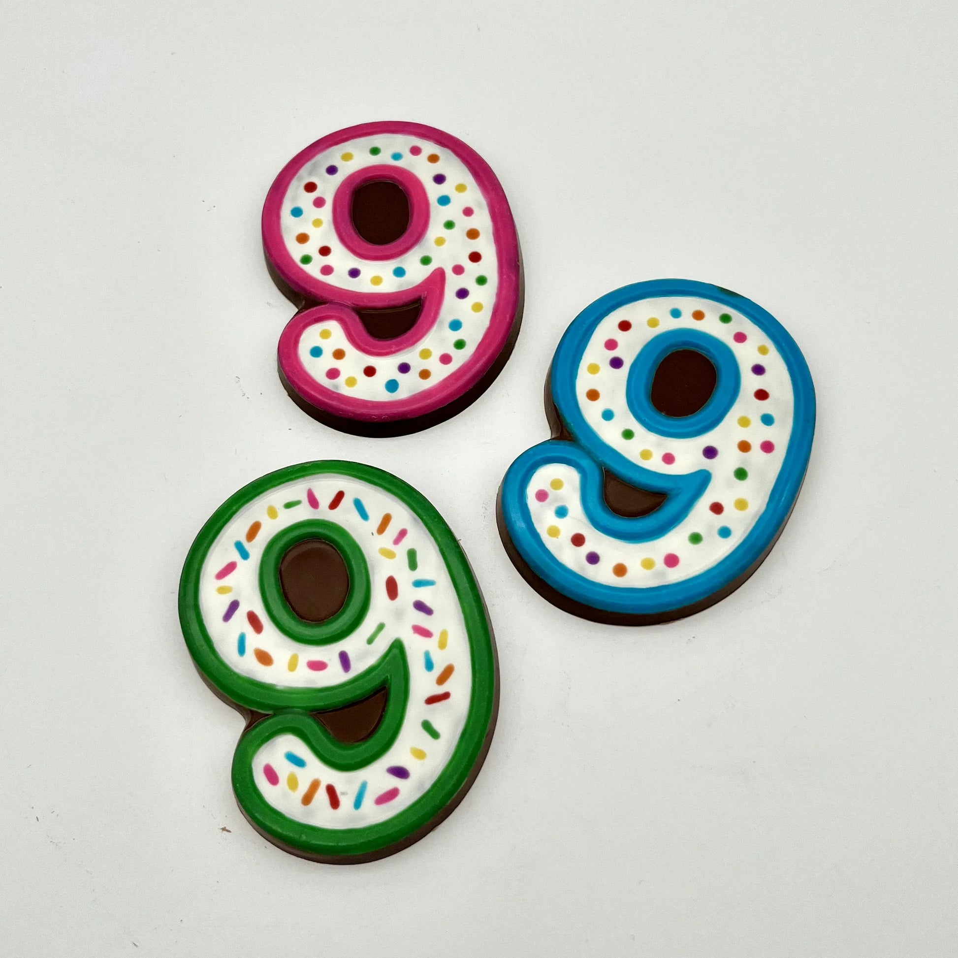 Three colourful number '9' chocolates, hand-painted with multi-colour dots and sprinkles. Displayed on a white background.