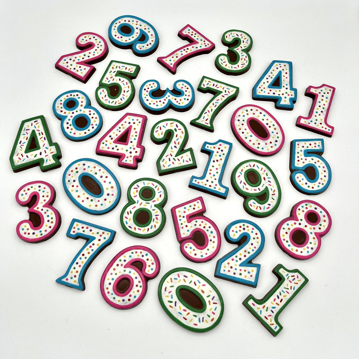 A multitude of colourful number chocolates, hand-painted with multi-colour dots and sprinkles. Displayed on a white background.