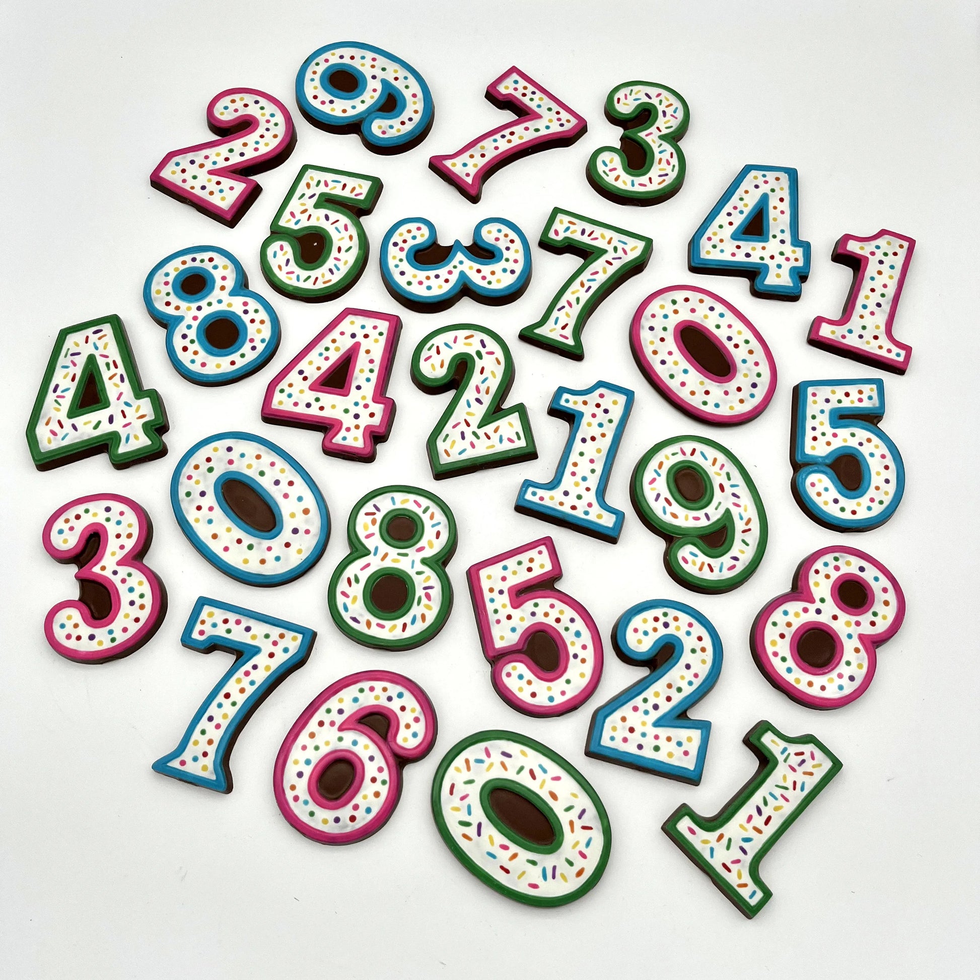 A multitude of colourful number chocolates, hand-painted with multi-colour dots and sprinkles. Displayed on a white background.